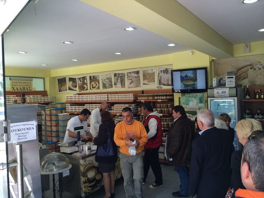man cutting Greek 'halva' with a knife at 'M. Kosmidis' store and people waiting to buy it